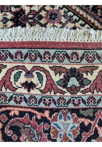 Close-up of a rolled Bijar Persian rug showcasing intricate patterns and vibrant colors. The rug features a dense weave with floral and geometric motifs in shades of red, blue, orange, and black on a pinkish-red background, with a soft, plush pile that offers a luxurious texture.