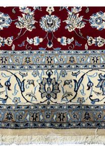 Macro shot focusing on the detailed floral and vine embroidery in the center of the Persian Nain 9La rug with highlights in silk, set against a deep red wool background