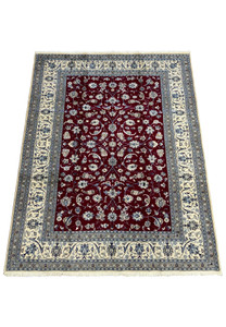 Full view of a Persian Nain 9La rug on the floor, showing the rich red center surrounded by ornate borders in cream and blue, emphasizing the rug's luxurious wool and silk blend