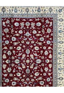 Wide angle of the entire Persian Nain 9La rug laid out, emphasizing its intricate floral motifs and the contrast of the cream and blue borders against the red center.