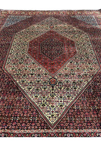 Angled perspective of a 9.8 x 12.2 Persian Bijar rug showing dense hand-knotted wool, rich red tones, ivory field sections, and the rug’s heavy iron-weave construction.