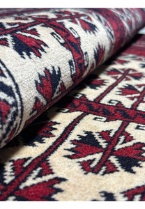 Rolled view of a 3'1 x 4'2 Persian Baluch rug, emphasizing the soft wool pile and the detailed star and geometric motifs in red, blue, and ivory