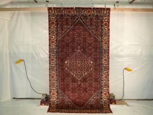 5'5 x 10 Persian Bijar Rug hanging for display, showcasing intricate crimson, navy blue, ivory, and green floral and geometric patterns