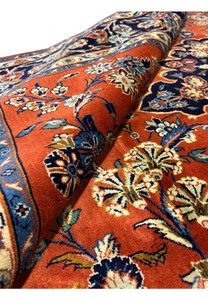 Close-up view of the 6'6 x 10'2 Persian Sarough Rug rolled to showcase the thickness and rich burnt orange color with intricate floral patterns.