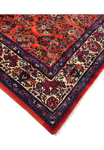 Persian Sarough rug corner with ivory floral border, navy guard stripes, and coral wool field filled with intricate floral sprays.