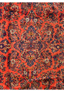 Persian Sarough rug medallion detail with intricate navy, ivory, and burgundy floral motifs on a coral wool background, fine hand-knotted design.