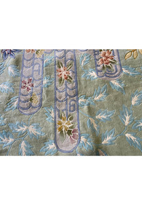 Macro photo of the Art Deco rug’s pastel floral patterns and curved lattice motifs in blue and lavender, accentuating the precision of the handwoven wool and color layering.