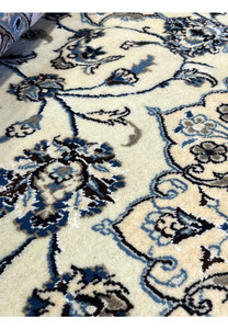 Close-up of Persian Nain 9LA Rug pattern showing navy and light-blue floral scrolls on ivory wool with silk accents.