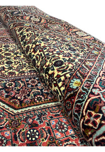 Rolled corner of Bijar Persian rug highlighting wool pile texture, strong knot density, and vibrant rust, ivory, and navy geometric medallion motifs.