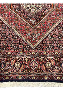 Close-up of lower border of Bijar Persian rug showing dense floral motifs, rust red background, and fine navy blue and ivory details.