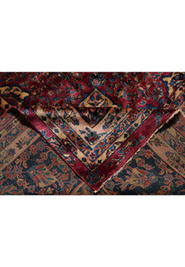Edge detail of antique Persian Kashan rug highlighting navy floral border, rose-red field, and aged wool patina with preserved original fringe ends.