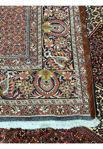 Close-up of the Bijar Persian Iron Rug border showing detailed floral motifs, rich brick red tones, cream fringe, and dense Kurdish weaving.