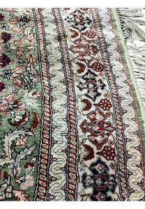 Border close-up of Qum pure silk rug showing layered floral bands, ivory and green tones, and delicate curvilinear motifs.