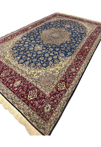 Angled perspective highlighting the shimmer of wool and silk across the blue field, medallion, and red borders.