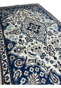 Angled view of Persian Nain rug highlighting royal navy blue field, ivory floral medallion, powder blue accents, and fine wool texture