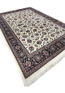 Angled view of signed Persian Mashad Saber rug showing ivory field and dense floral design