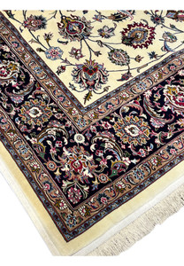 Angled view of signed Persian Mashad Saber rug showing ivory floral field and dark navy botanical border with fine wool detailing
