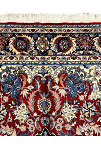 Upper end border detail of Persian Tabriz rug with navy floral border band, ivory accents, and fringe at the top