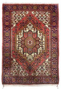 Hand-knotted Persian Gholtogh rug with bold geometric medallion, brick red field, ivory accents, and navy tribal border, full view