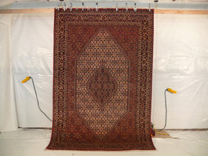 Hanging view of a 6'5 x 10 authentic Persian Bijar rug showing its firm iron rug structure, dense wool pile, crisp medallion design, and rich red color tones