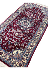Angled perspective of a Persian Tabriz medallion rug highlighting pile texture, color depth, and the contrast between burgundy field and ivory borders