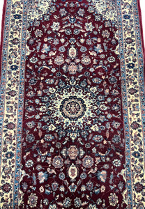 Close view of the central medallion on a Persian Tabriz rug showing ivory and navy detailing, fine knotting, and dense floral symmetry on a burgundy field.