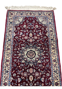 Midfield detail of a Persian Tabriz rug featuring layered floral motifs, soft blue and blush accents, and dense hand-knotted wool on a burgundy ground