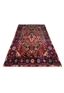 Laid flat view of a Persian Gholtogh rug showing strong geometric medallion, deep red ground, navy framing, and expressive tribal patterning