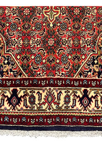 Lower border view of a Persian Bijar rug featuring layered framing, deep red tones, floral rosettes, and strong visual definition
