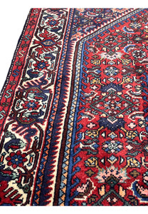 Angled side view of hand-knotted Persian Gholtogh rug highlighting dense wool pile, crisp tribal patterns, and rich red and navy color contrast