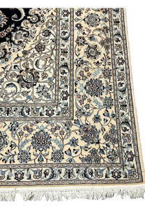 Border close-up of a Persian Nain Habibian rug showing intricate floral bands with ivory ground, pale blue blossoms, and fine navy outlining