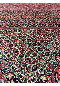 Inner border closeup of a Persian Bijar rug highlighting repeating geometric motifs, ivory background, red accents, and precise high-density wool weaving