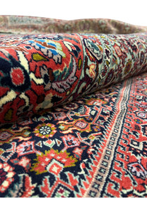 Rolled edge view of a 9x13 Persian Bijar iron rug showing dense wool pile, deep red field, navy blue details, and tightly packed geometric motifs