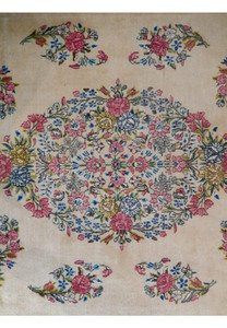 Close-up of the central medallion on a Persian Kerman rug showing layered floral clusters in pink, light blue, soft green, and pale yellow tones