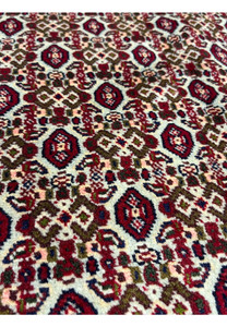 Herati inspired detail in Persian Senneh rug showing stylized rosettes, angular leaves, burgundy field, and ivory lattice definition