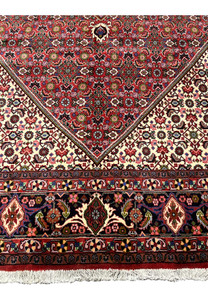 Lower border of Persian Bijar rug displaying dense floral motifs, rich red tones, navy accents, and clean hand knotted execution