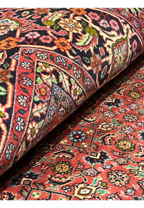 Persian Bijar all-over rug partially rolled to display rich terracotta field, navy border, and intricate floral motifs