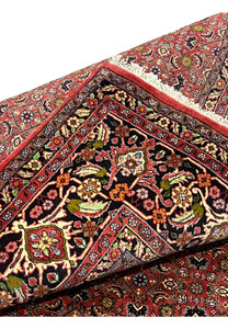 Folded edge of Persian Bijar rug revealing plush wool pile, crisp floral design, and flexible yet dense structure