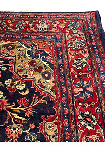 Top border detail of handmade Mahal rug with bold red ground, ivory palmettes, scrolling vines, and fine blue guard stripes along the edge