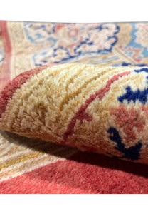 Macro wool pile closeup revealing dense hand knotted craftsmanship, soft fibers and warm gold, cream and red tones