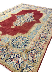 Persian Kerman rug angled view showing brick red field, ivory floral border, navy medallion and soft sky blue panels in hand knotted wool