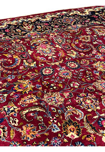 Design closeup of Persian Mashad rug showing symmetrical floral layout, brick red field, multicolor blossoms, and classic Persian composition.