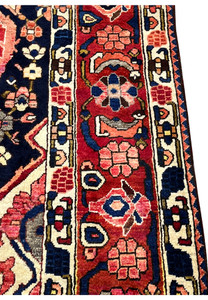 Close-up of main border on vintage Persian Bakhtiari rug with repeating floral heads on crimson red ground.