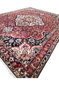 Angled view of Persian Bakhtiari rug 10x14 with ivory medallion on crimson red wool field.