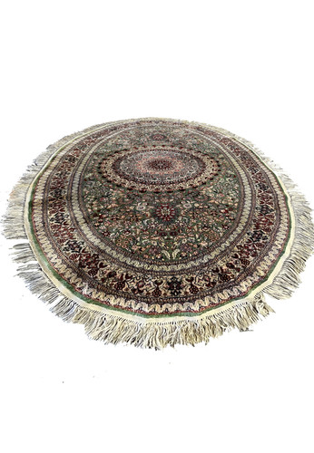 Oval Persian Qum pure silk rug laid flat, showing detailed floral medallion, fine knotting, and shimmering green, ivory, and burgundy tones.