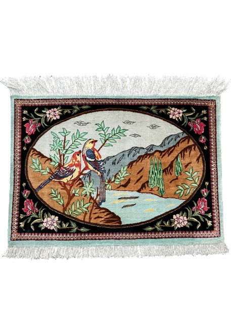 A Persian Qum silk rug with a pictorial design of two birds on a branch, surrounded by a floral border and fringe edges.