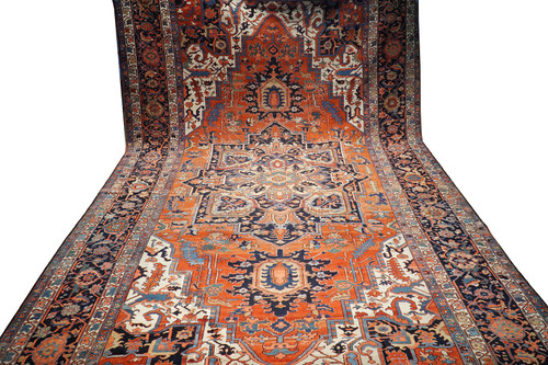 11'2" x 19'1" antique Persian Serapi rug hung full length showing rust field and navy borders