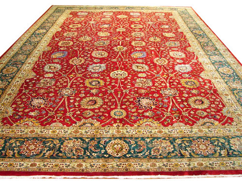 Angled studio view of red Persian Tabriz rug with emerald green floral border and ivory guards