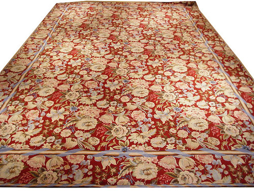 Burgundy needlepoint rug with ivory roses and pale blue ribbon border shown on a raised platform