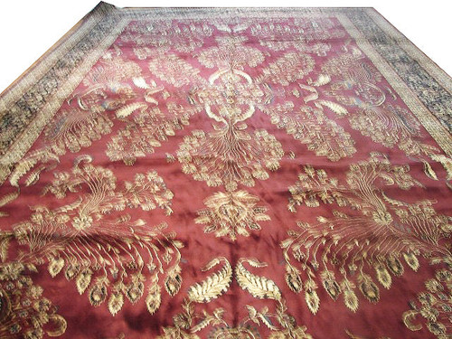 Oversize burgundy Sarouk design rug photographed at an angle showing ivory floral sprays and navy border